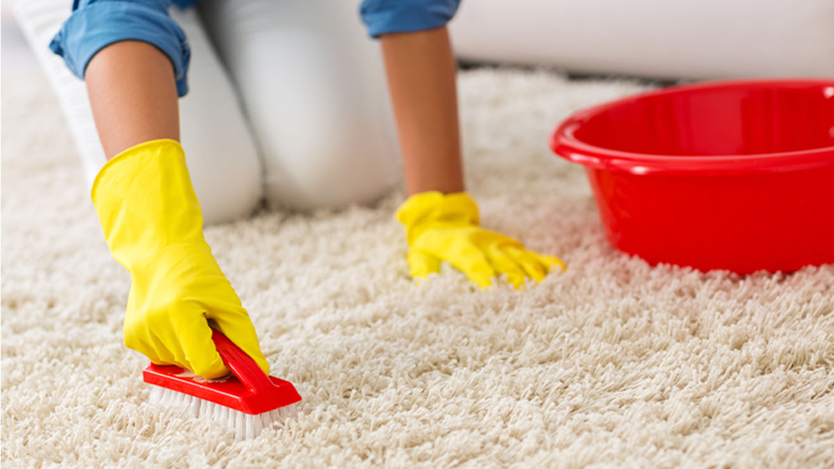 Mulher com luvas amarelas a lavar carpete com produtos de limpeza de carpetes e tapetes